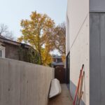 Arthur Residence 옆 통로, 콘크리트 벽 사이에 카누와 정원 도구가 놓여 있다