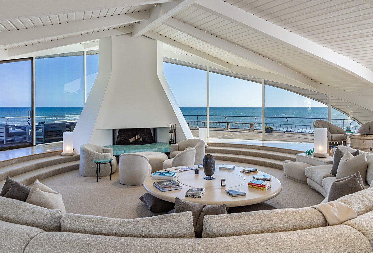 곡선 천장 아래 원형 소파와 벽난로가 놓인 Wave House 거실