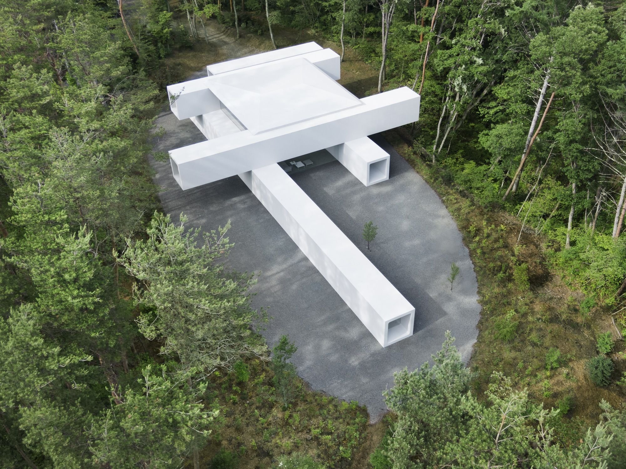 숲속 자갈 마당 위에 콘크리트 박스를 십자로 쌓은 Culvert Guesthouse 항공 전경