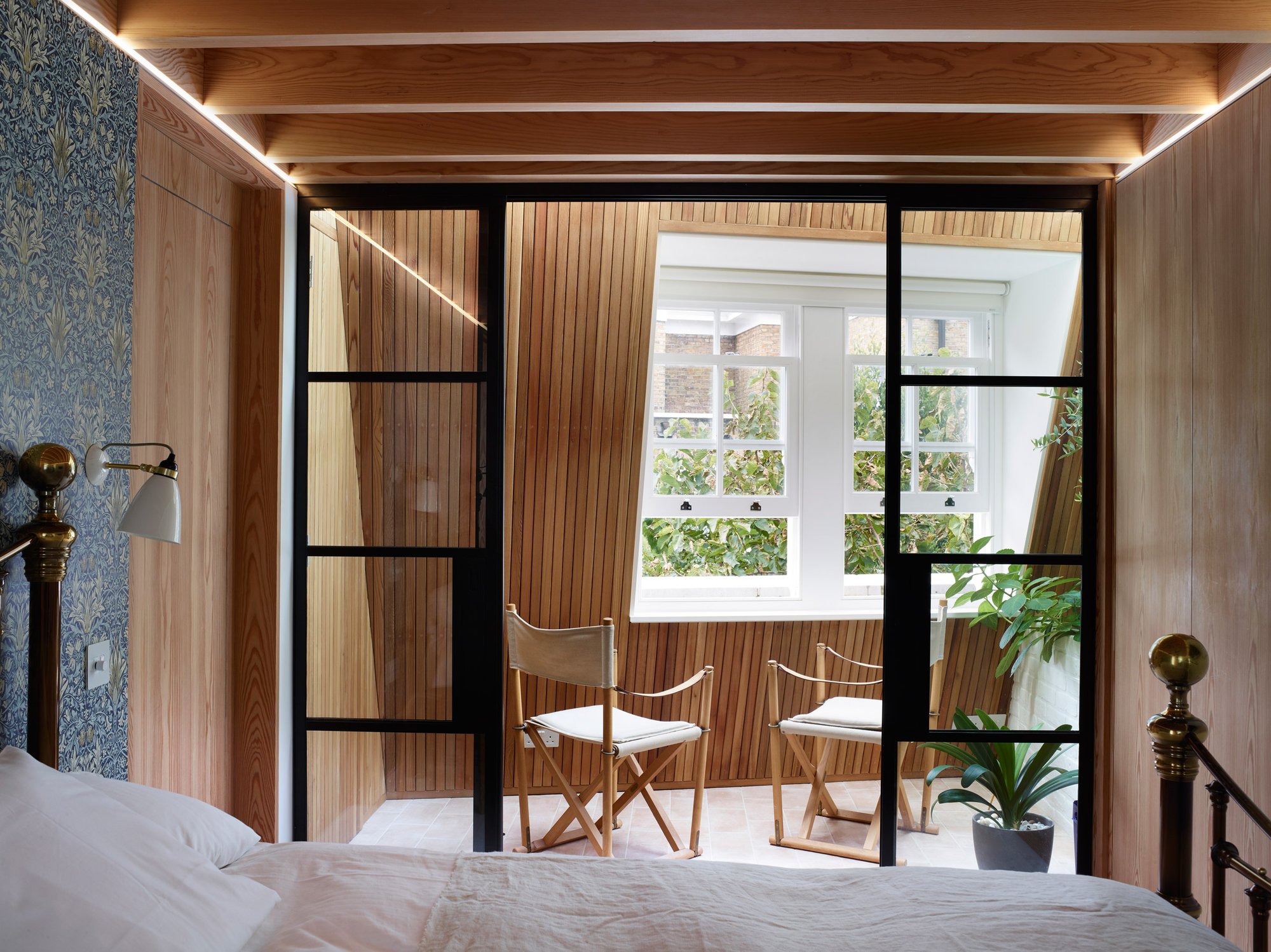 블랙 프레임 유리문 너머 테라스로 이어지는 Danish Mews House 침실