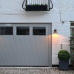 그레이 차고 문과 벽등이 켜진 Danish Mews House 1층 외관