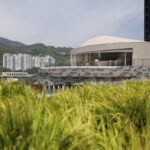 옥상 풀숲 너머로 보이는 곡면 Sky House 외관과 주변 산