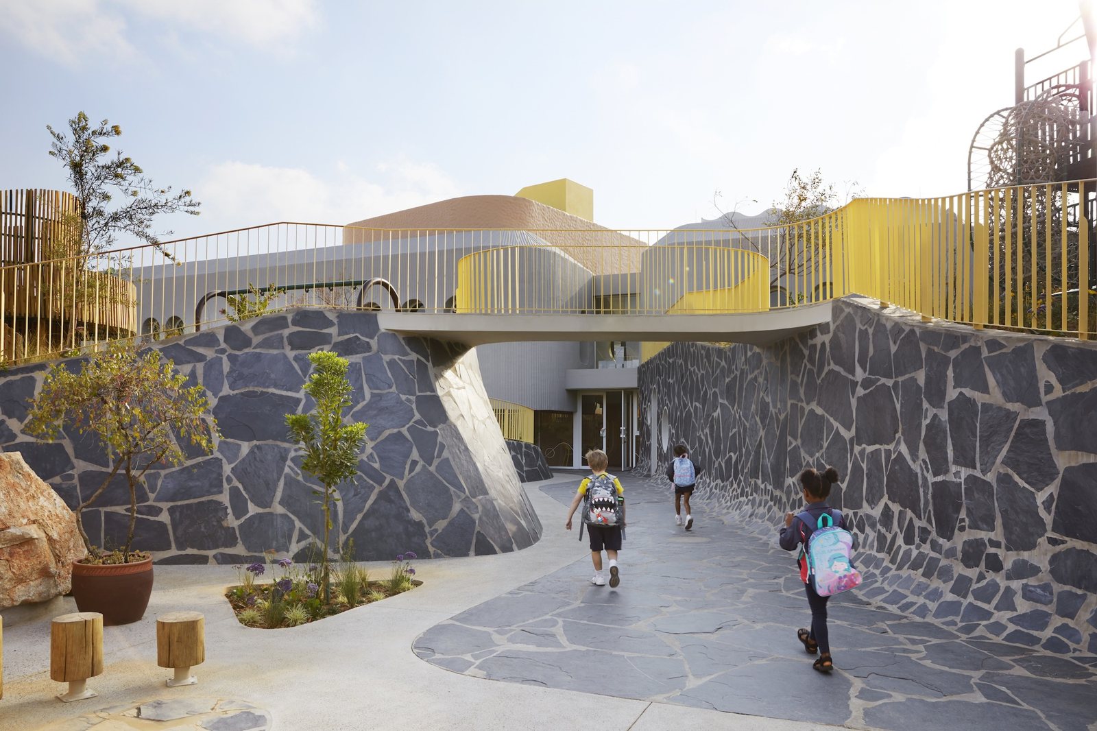슬레이트 옹벽 사이 길로 아이들이 걸어 들어가는 Redhill Early Learning Centre 진입로