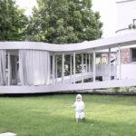 잔디밭을 걷는 아이 뒤로 보이는 Ring House 곡선 파빌리온 외관