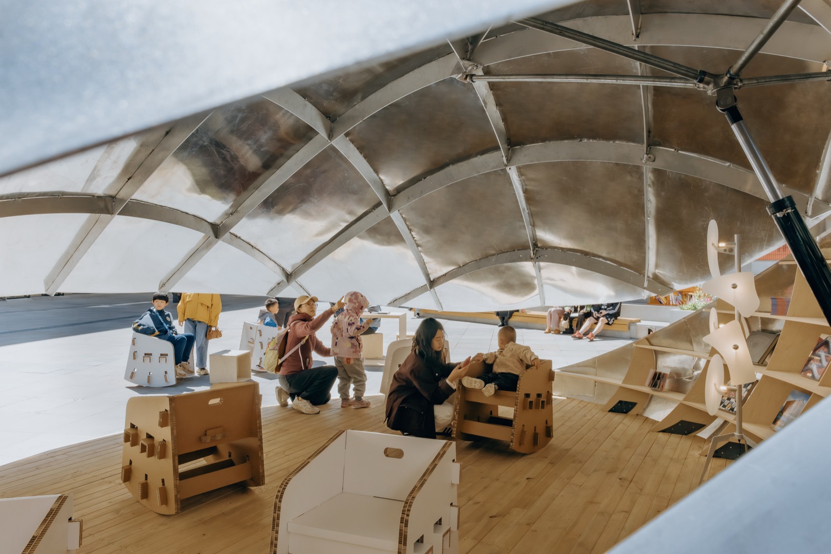 알루미늄 리브가 드러난 Shell Book Pavilion 지붕 안쪽과 책 읽는 아이들