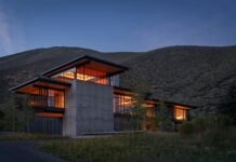 해 질 녘 산을 배경으로 콘크리트 타워와 유리 거실이 빛나는 미국 산장 Sky View