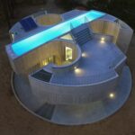 해 진 뒤 옥상 수영장에 불이 켜진 Trefoil House 콘크리트 주택 항공 전경