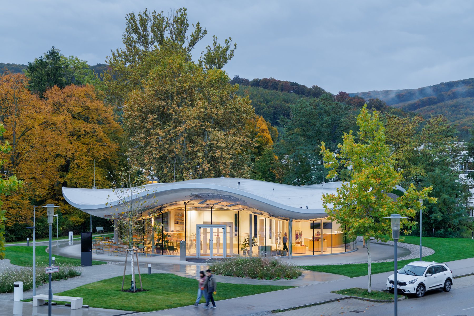 해 질 녘 숲을 배경으로 실내 불빛이 번지는 VISTA Science Experience Center 외관