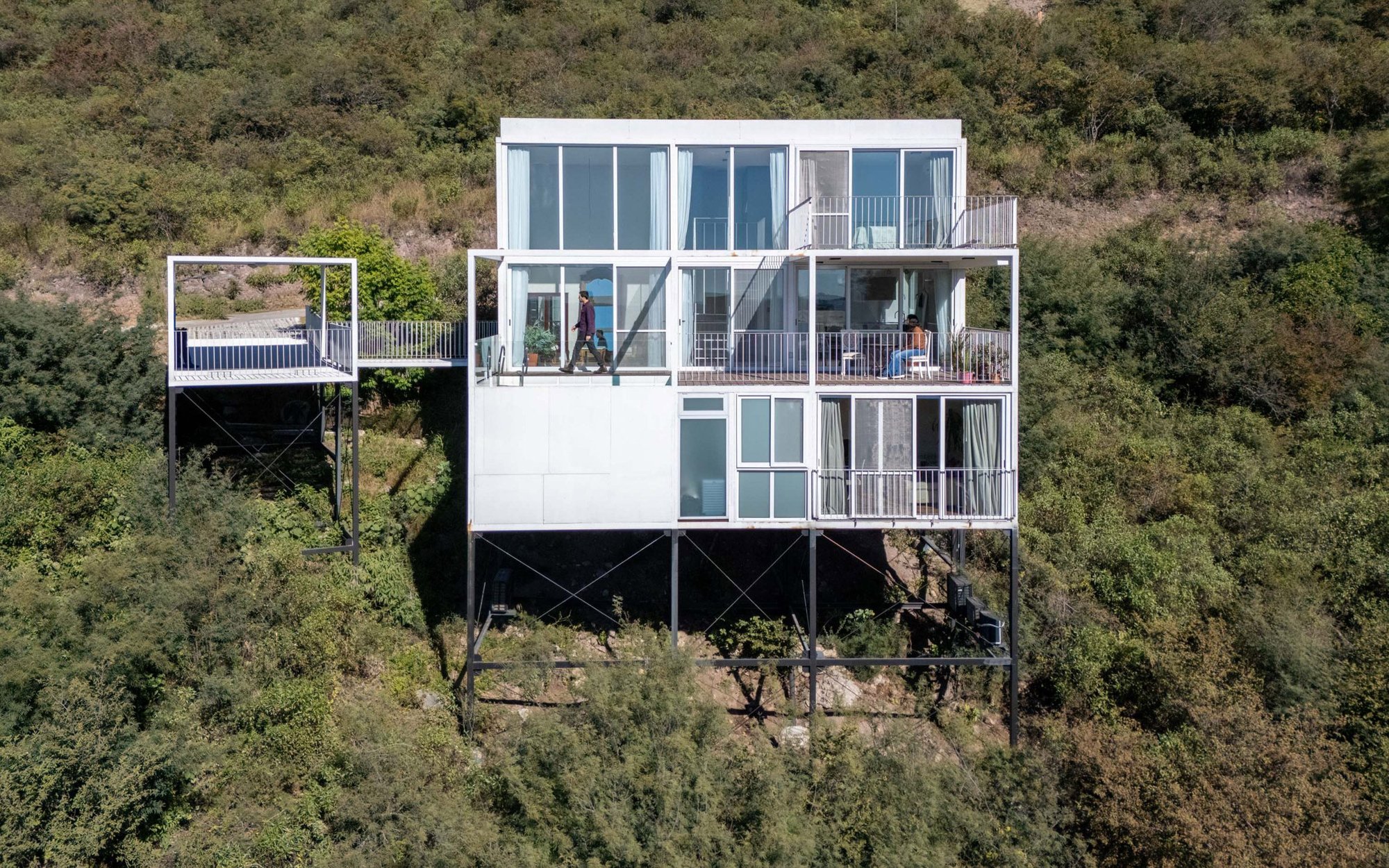 가는 철골 기둥 위에 올라선 White Modular House 정면 외관과 경사지